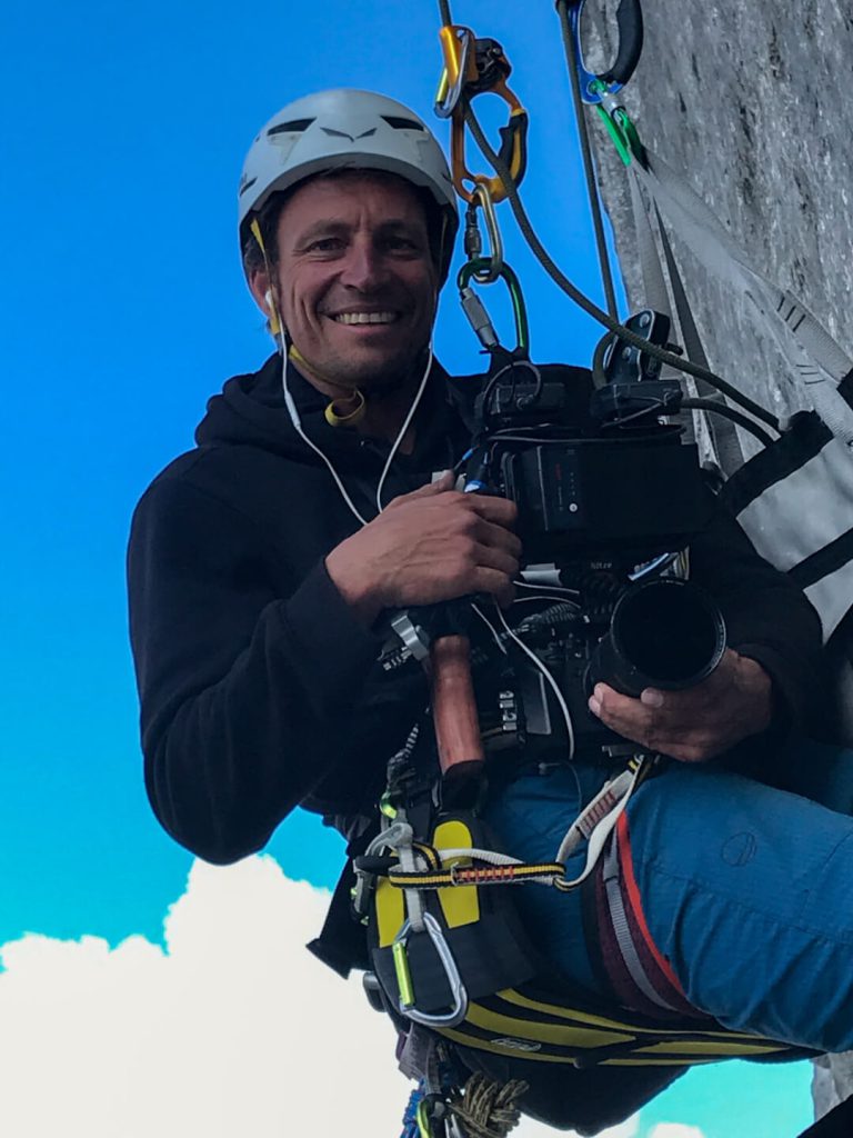Kameramann mit Helm und Kletterausrüstung filmt an Felswand, professionelle Luftaufnahmen
