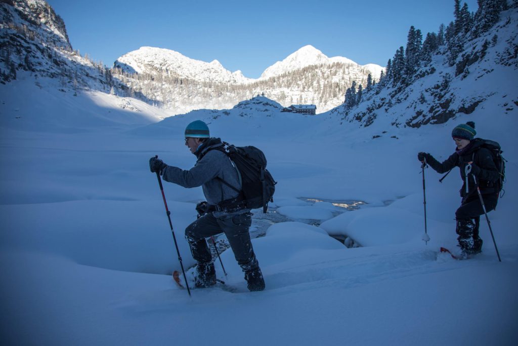Zwei Menschen mit Schneeschuhen wandern durch verschneite Winterlandschaft vor Alpenpanorama