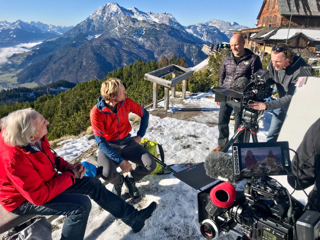 Drehteam filmt Interview auf verschneiter Berghütte mit Alpenpanorama für professionelle Videoproduktion