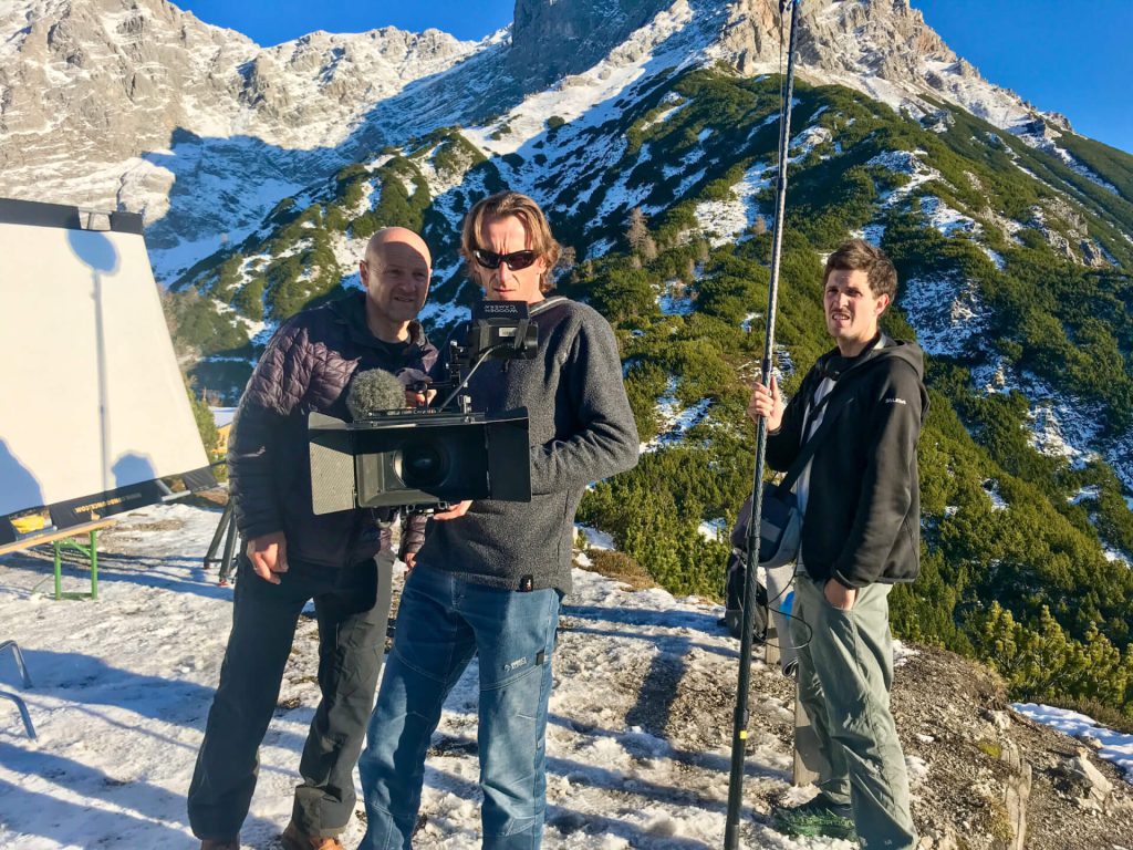 Filmteam mit Kamera und Tonangel bei Videoproduktion im verschneiten Gebirge, Luftaufnahmen