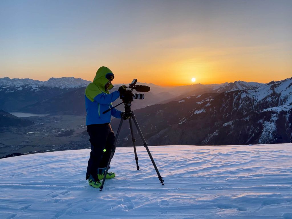 Kameramann filmt bei Sonnenaufgang auf verschneitem Berg Panorama, professionelle Luftaufnahmen