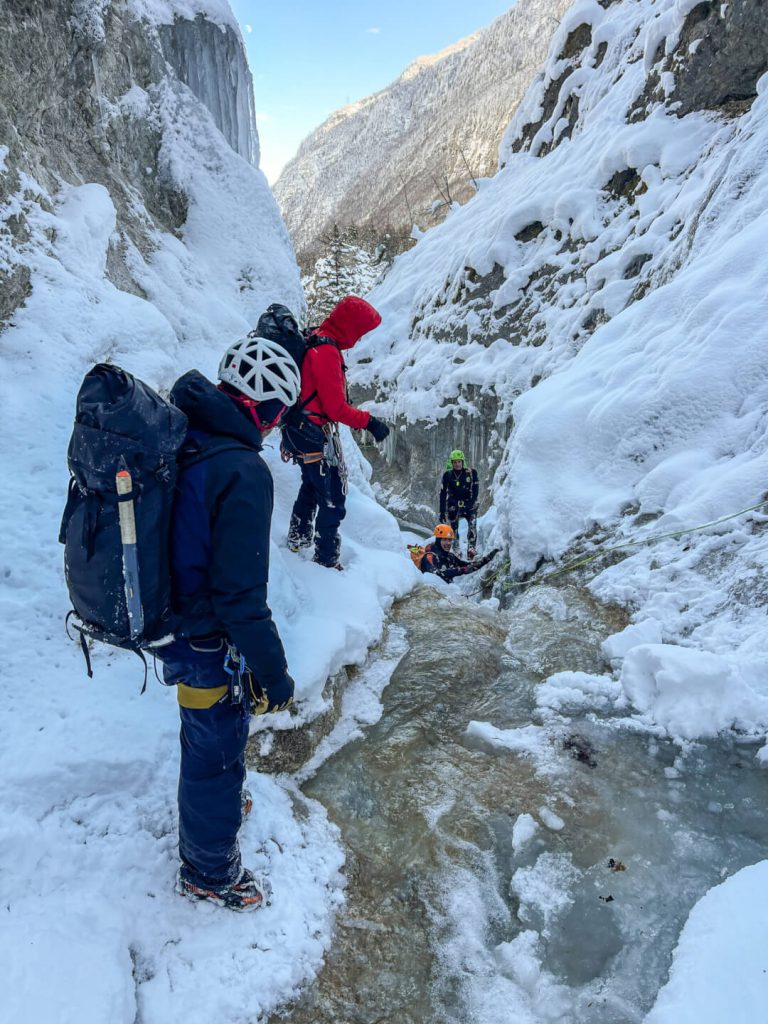 Vier Bergsteiger mit Ausrüstung beim Winterklettern in verschneiter Schlucht, Drohnenaufnahme
