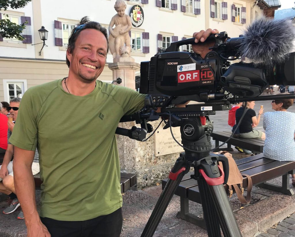 Kameramann mit professioneller Filmkamera auf Stativ, Videoproduktion im urbanen Außenbereich