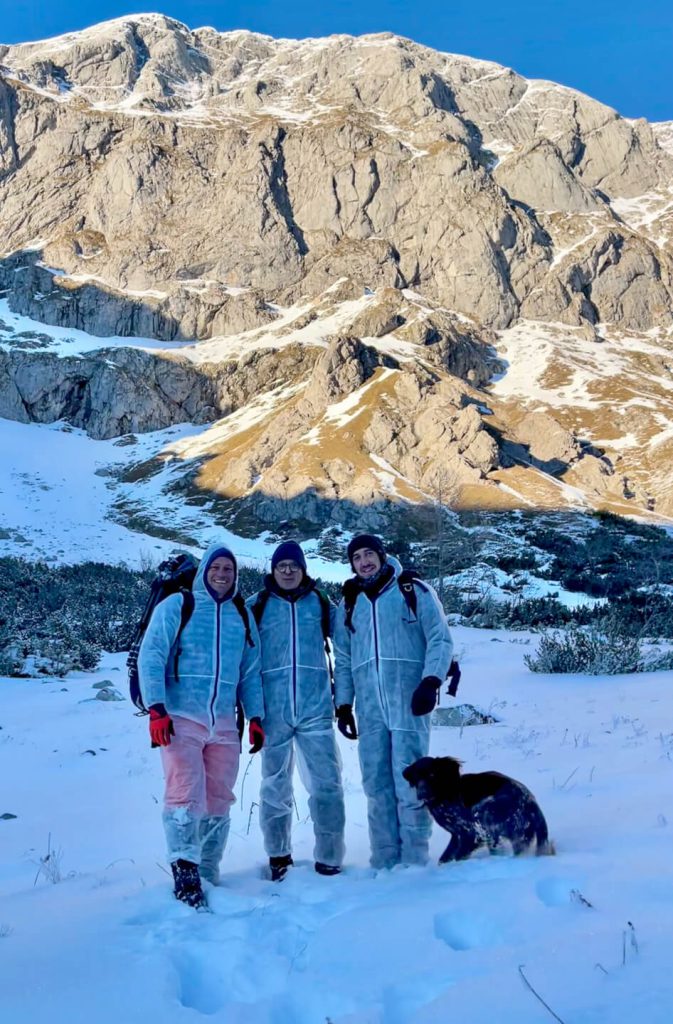 Drei Personen und ein Hund in Winterlandschaft, verschneite Berge, Outdoor- und Naturerlebnis