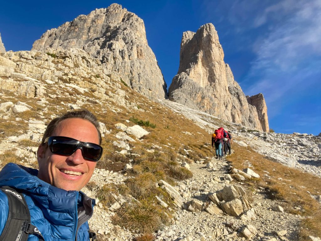 Wanderer mit Sonnenbrille im Vordergrund, Gruppe auf steinigem Pfad vor markanten Felsen